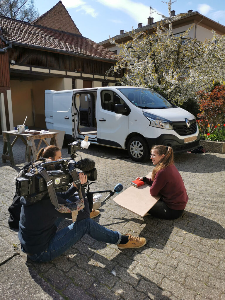 Reportage TF1 sur l'aménagement d'un van à Strasbourg avec interview d'une artisane ébéniste de Cosy van devant un Renault Trafic en cours d'aménagement