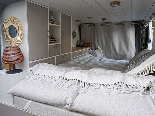 Lit escamotable avec rangements intégrés dans un fourgon aménagé pour la vanlife.