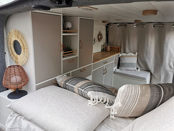 Vue intérieure d'un van aménagé sur mesure avec des meubles en bois. Décoration esprit plage pour des roadtrips en couple en Alsace.