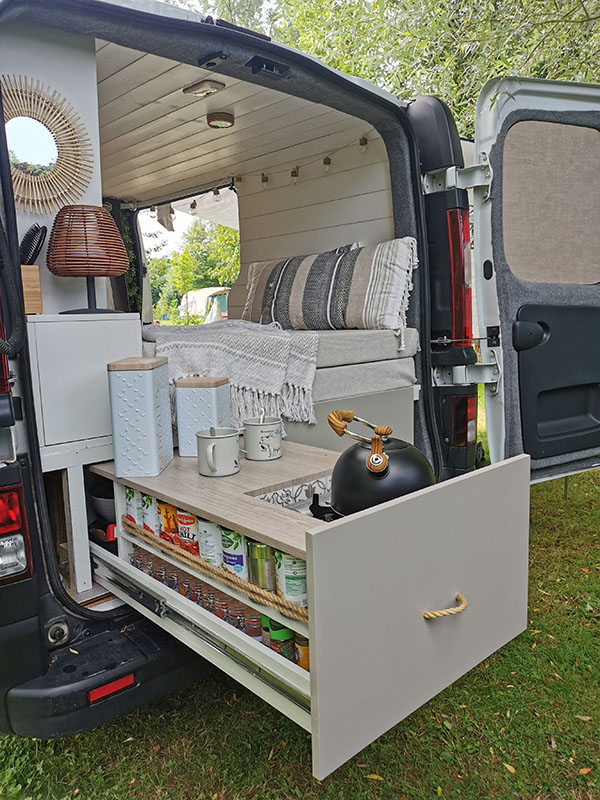 Cuisine extérieure d'un Renault Trafic aménagé avec gazinière et de multiples rangements pour cuisiner.