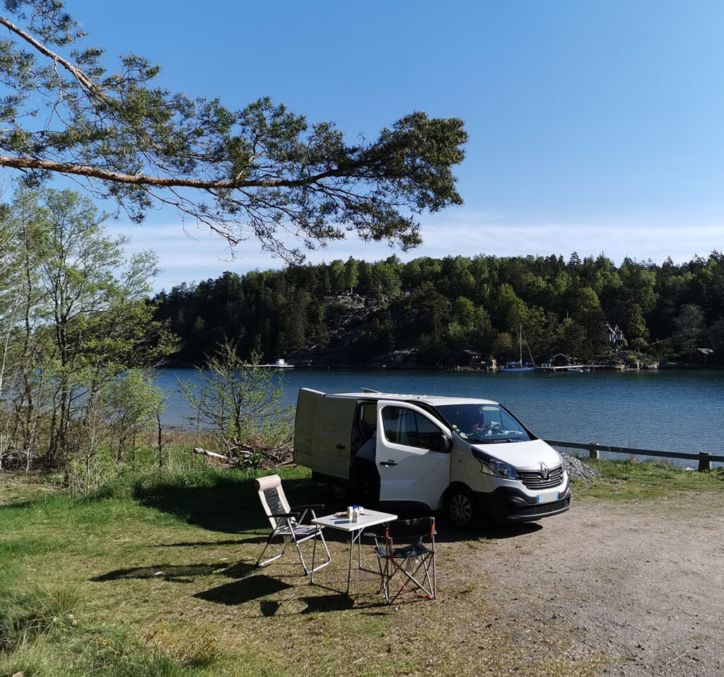 Van aménagé (Renault Trafic) par Cosy Van au bord d'un lac en Suède avec une table et des chaises de camping.
